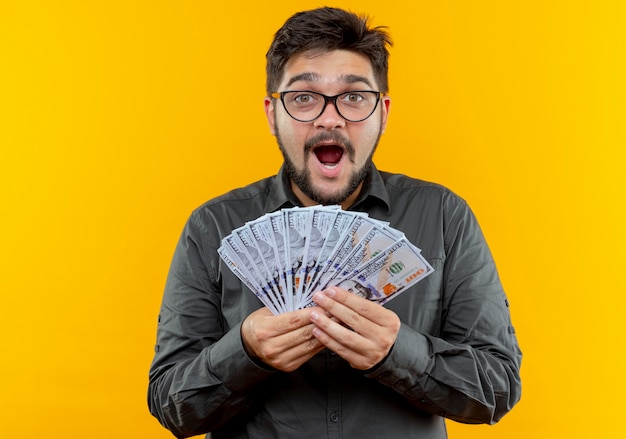 Foto grátis jovem empresário alegre usando óculos, segurando dinheiro isolado em um fundo amarelo