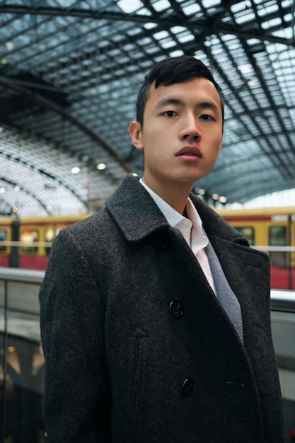 Foto grátis jovem empresário asiático estiloso de casaco olhando com confiança para a câmera na estação de metrô