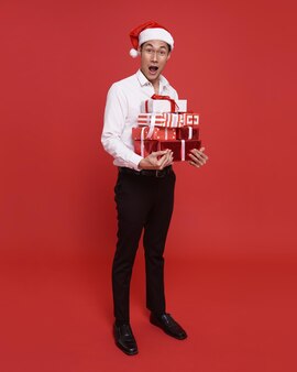 Jovem empresário asiático usando chapéu de papai noel e segurando uma caixa de presente na festa de natal e feliz ano novo