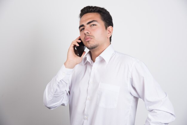 Jovem empresário com celular posando em fundo branco.