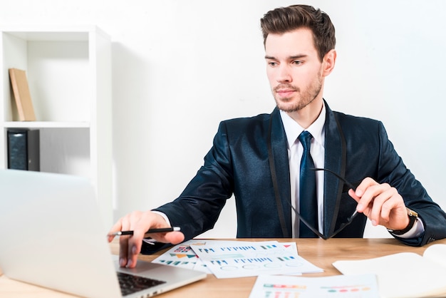 Jovem empresário confiante usando o laptop no local de trabalho no escritório