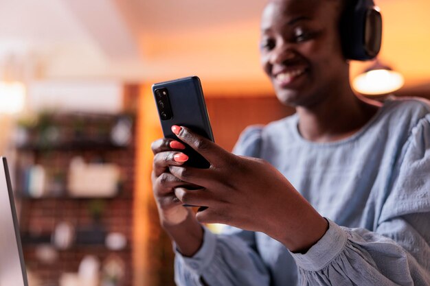 Jovem empresário conversando online e digitando mensagem no smartphone. Mulher sorridente freelancer americano africano falando na internet usando telefone celular no escritório doméstico moderno