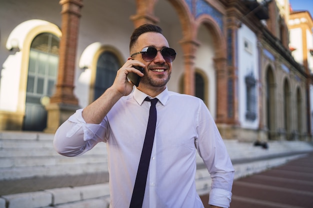 Jovem empresário de sucesso com uma roupa formal e óculos de sol falando ao telefone