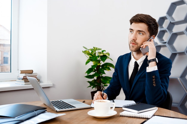 Jovem empresário de sucesso falando no telefone, plano de fundo do escritório.