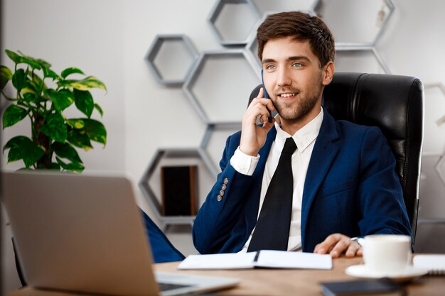 Jovem empresário de sucesso falando no telefone, plano de fundo do escritório.