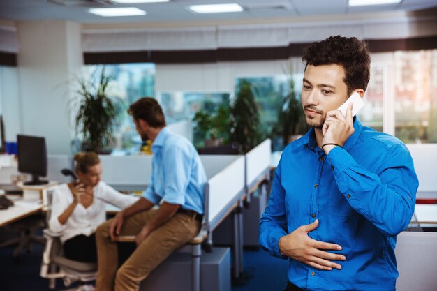 Jovem empresário de sucesso, falando no telefone, sorrindo, sobre o escritório