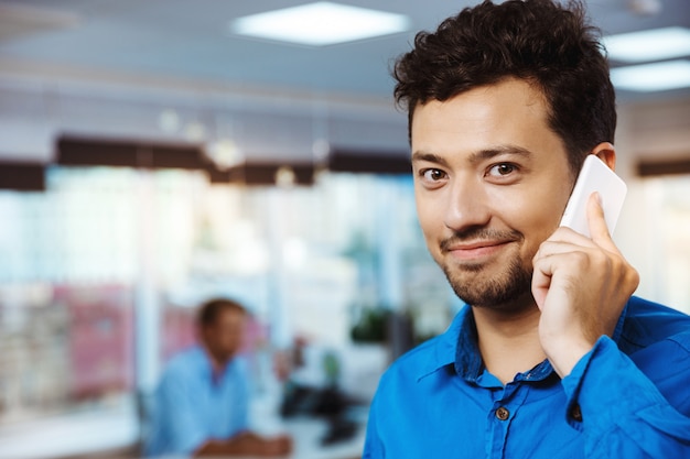 Jovem empresário de sucesso, falando no telefone, sorrindo, sobre o escritório