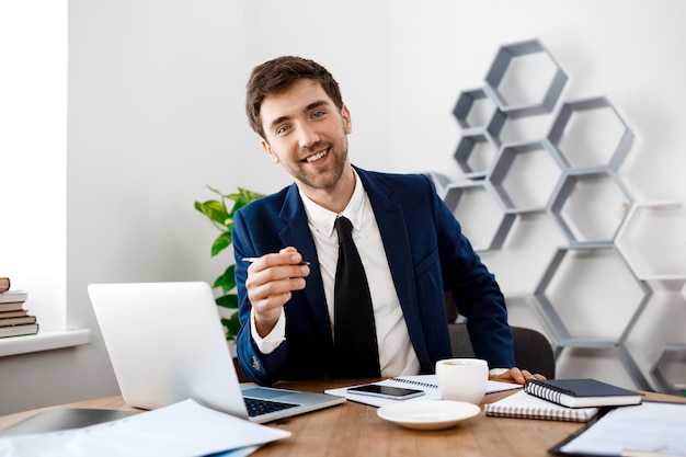 Foto grátis jovem empresário de sucesso sentado no local de trabalho, plano de fundo do escritório.