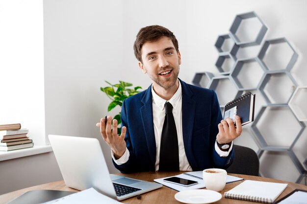 Jovem empresário de sucesso sentado no local de trabalho, plano de fundo do escritório.