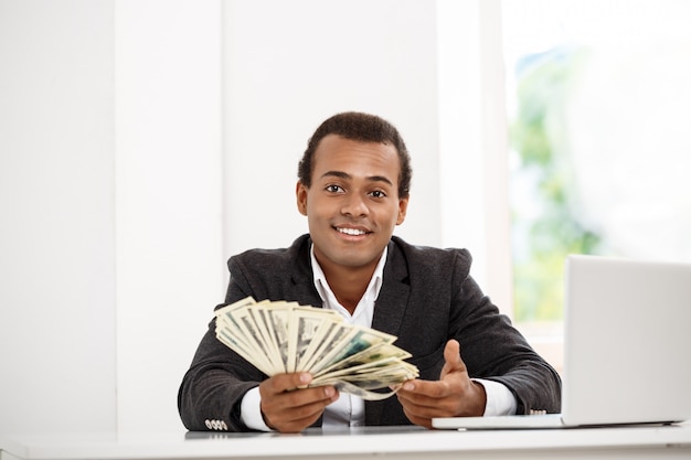 Jovem empresário de sucesso, sorrindo, segurando o dinheiro, sentado no local de trabalho