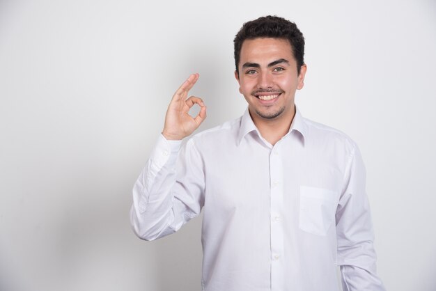 Jovem empresário fazendo sinal de ok com uma mão no fundo branco.