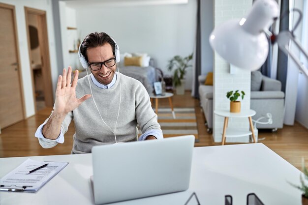 Jovem empresário feliz acenando enquanto tem reunião online sobre laptop de casa