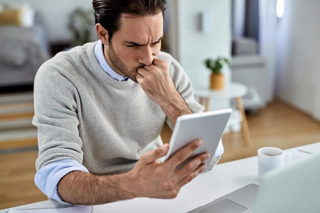 Jovem empresário perturbado trabalhando em casa e lendo e-mail problemático no tablet digital