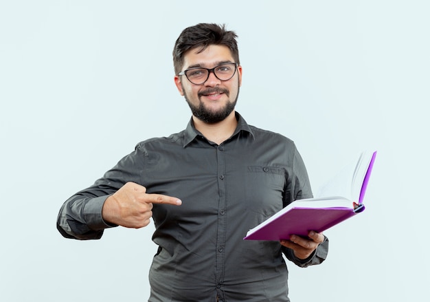 Jovem empresário satisfeito usando óculos segurando e apontando para um livro isolado no fundo branco