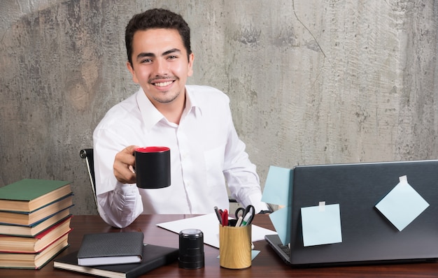 Jovem empresário segurando uma xícara de chá na mesa do escritório.