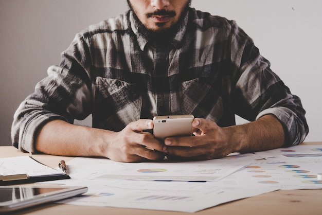 Jovem empresário sentado e usando o telefone móvel no local de trabalho no escritório. Homem de negócios fazer exame de uma ruptura ao trabalhar a análise com dados do negócio.