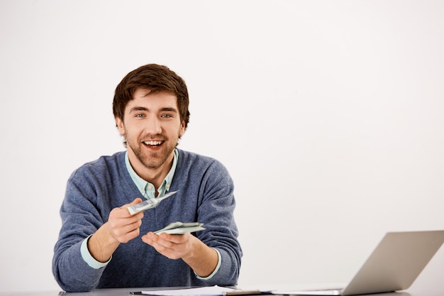 Jovem empresário sorridente dar dinheiro, sentar na mesa com o laptop, contando dinheiro, dar metade da renda ao parceiro de negócios