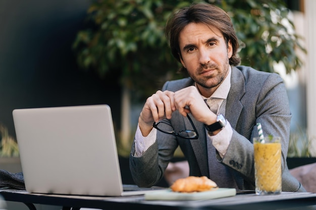 Jovem empresário trabalhando no laptop e olhando para a câmera enquanto está em um café