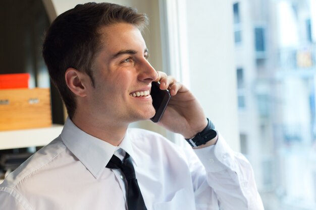 Jovem empresário usando seu celular no escritório.