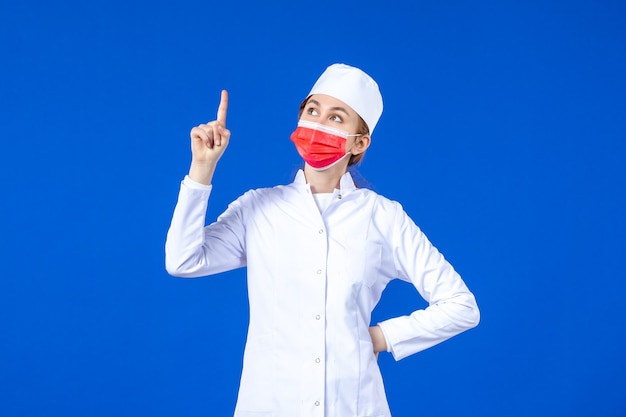 Jovem enfermeira de frente para um terno médico com máscara protetora vermelha na parede azul