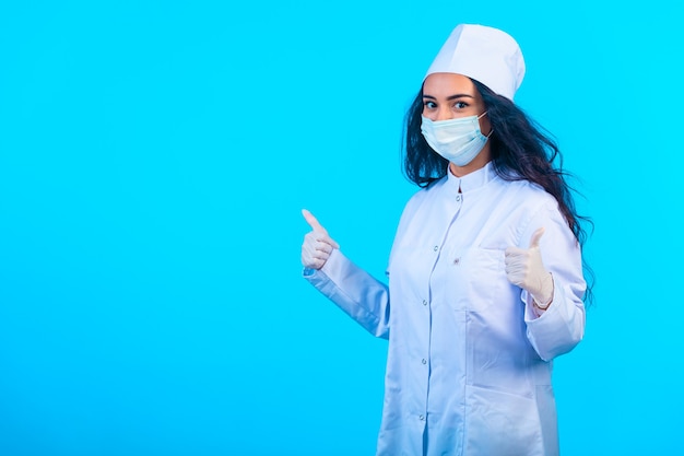 Jovem enfermeira em uniforme isolado segurando fazendo polegares para cima sinal de mão.