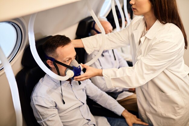 Jovem enfermeira verificando a máscara de um paciente durante a oxigenoterapia hiperbárica na clínica médica