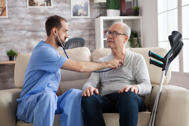 Jovem enfermeiro com estetoscópio ouvindo o coração do homem sênior no lar de idosos.