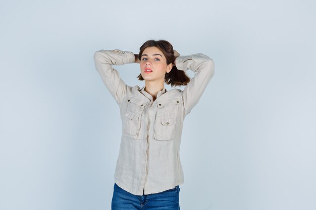 Jovem, enfiando o cabelo com as mãos em uma camisa bege, jeans e linda. vista frontal.