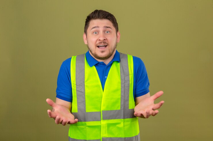 Foto grátis jovem engenheiro usando colete de construção, parecendo sem noção e confuso, tendo dúvidas sobre fundo verde isolado