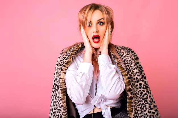 Jovem engraçada surpresa chocada mulher posando em fundo rosa, vestindo camisa branca e casaco de leopardo, emoções poderosas.