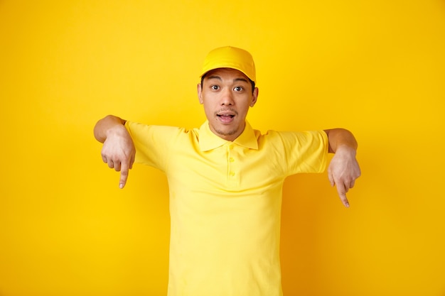 Jovem entregador animado usando boné e uniforme apontando para baixo