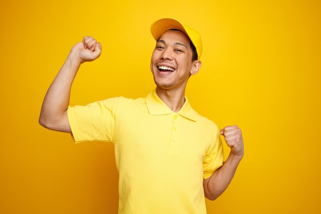 Jovem entregador animado usando boné e uniforme cerrando os punhos cerrados