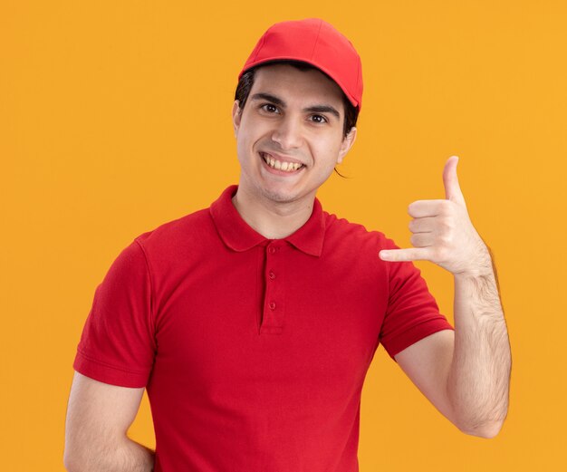 Jovem entregador caucasiano sorridente com uniforme azul e boné, mantendo a mão atrás das costas fazendo gesto de pendurar