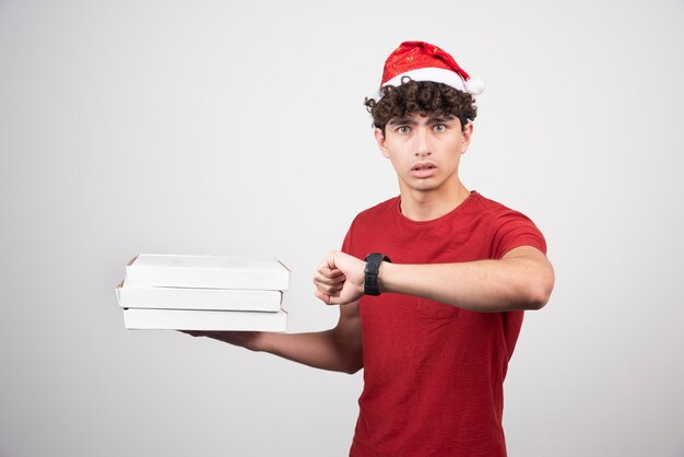 Jovem entregador com caixas de pizza, verificando a hora.