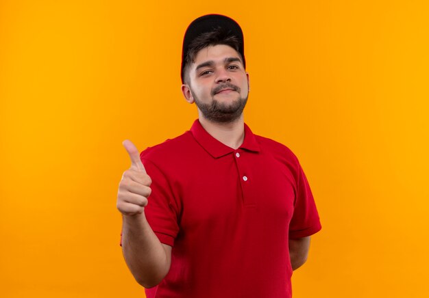 Jovem entregador de uniforme vermelho e boné sorrindo, mostrando os polegares para cima