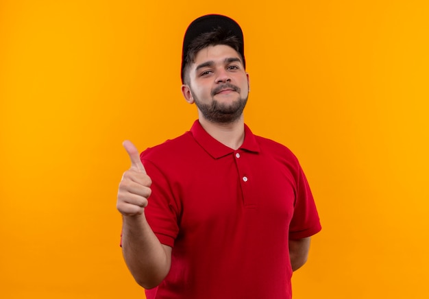 Jovem entregador de uniforme vermelho e boné sorrindo, mostrando os polegares para cima