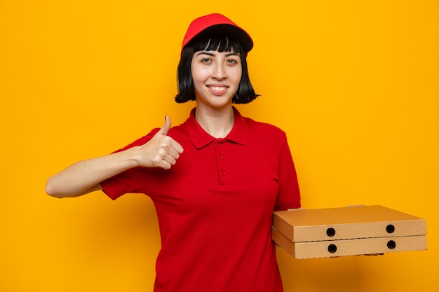 Jovem entregadora caucasiana satisfeita segurando caixas de pizza e dedilhando