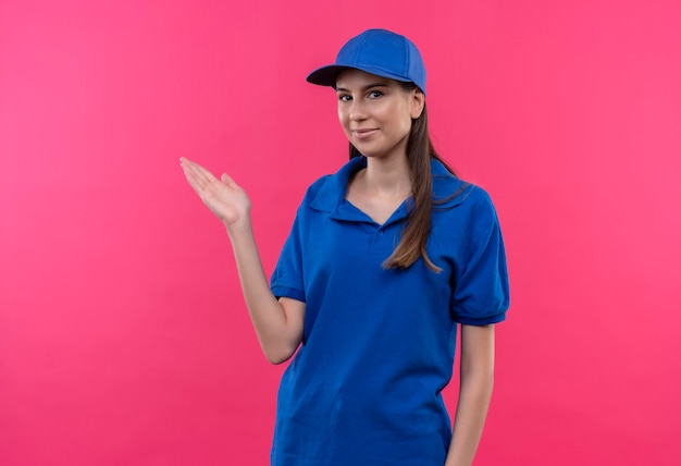 Jovem entregadora de uniforme azul e boné, apresentando-se com um braço da mão, copie o espaço