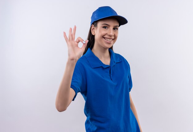 Jovem entregadora de uniforme azul e boné sorrindo confiante mostrando sinal de ok