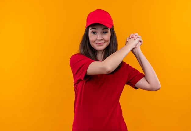 Jovem entregadora vestindo camiseta vermelha com boné vermelho sorrindo e aperto de mão em fundo amarelo isolado