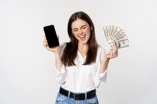 Foto grátis jovem entusiasmada ganhando dinheiro mostrando interface de aplicativo para smartphone e prêmio de microcrédito em dinheiro...