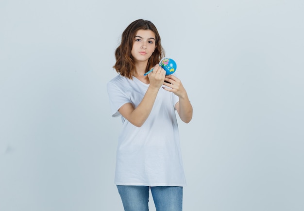 Jovem, escrevendo na globo com lápis, segurando uma camiseta, jeans e olhando com foco. vista frontal.