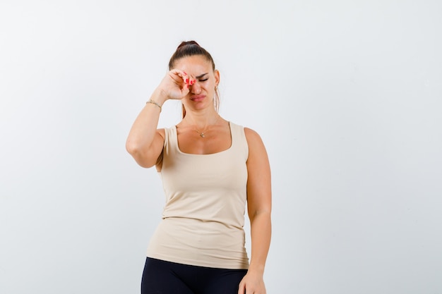 Jovem, esfregando os olhos enquanto chorava de top e parecendo deprimida, vista frontal.