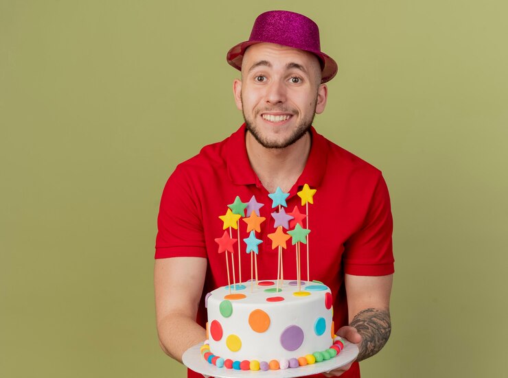 Foto grátis jovem eslavo bonito sorridente com um chapéu de festa segurando um bolo de aniversário, olhando para a câmera, isolada em um fundo verde oliva com espaço de cópia