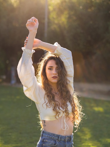 Jovem espanhola de cabelos compridos posando no parque primavera com os braços para cima