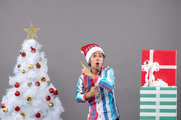 Jovem espantado de frente com um chapéu de Papai Noel em espiral mostrando a árvore de natal branca
