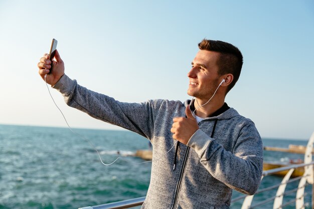 Jovem esportiva em fones de ouvido e jaqueta esporte, mostrando um polegar para cima