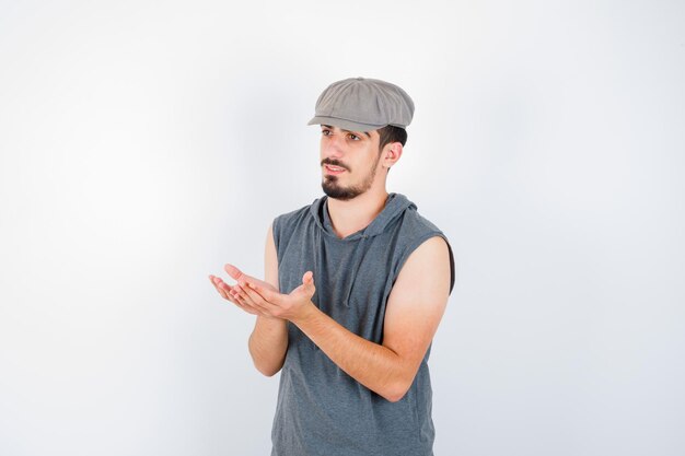 Jovem, estendendo a mão e segurando algo com uma camiseta cinza e boné, parecendo sério