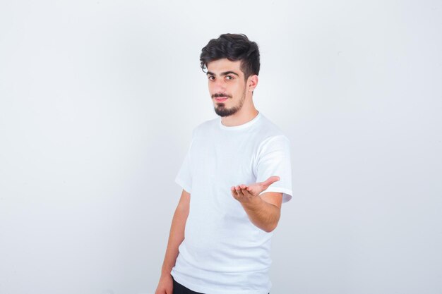 Jovem esticando a mão para mostrar algo em uma camiseta branca e parecendo confiante