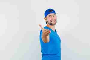 Foto grátis jovem esticando a mão para um aperto de mão usando camiseta azul e boné, parecendo feliz